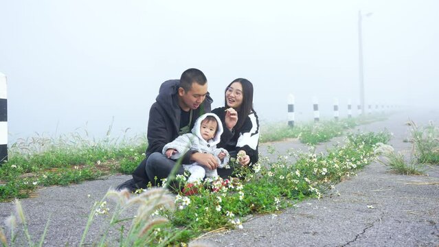 4K, happy family in morning with cold weather and fog covering area, father mother take their cute little daughter come see fog feel thick air, and sit admire flowers found in tourist attractions.