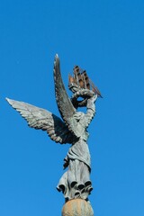 Angel with wings stands on ball at top of column with sailboat in raised hands. Close-up. Column "Sea Glory of Russia" on embankment of Admiral Serebryakov. Novorossiysk, Russia - December 20, 2022