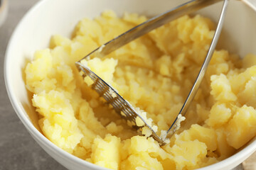Bowl with delicious mashed potato and masher on light grey table, closeup