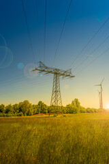 Beautiful farm landscape and industrial high voltage power line pylons and wind turbines farm at sunset warm colors and direct sun light with lens flare and sun rays in Germany