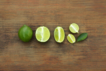 Whole and cut fresh ripe limes with green leaf on wooden table, flat lay