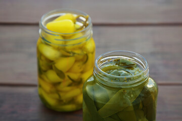 Glass jars of pickled green and yellow jalapeno peppers on wooden table, closeup