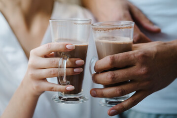 The couple is drinking cacao sitting at the cafe. Young beautiful couple hugging at the restaurant's summer terrace in casual clothes with a latte in their hands. Man and woman resting.