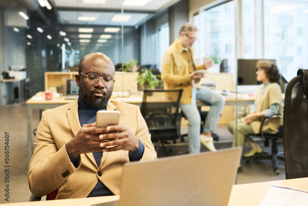 Aufkleber serious african american manager using smartphone while sitting by workplace in front of laptop and 