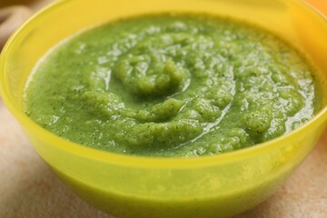 Baby food. Bowl with tasty broccoli puree on beige textured table, closeup