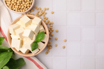 Delicious tofu cheese, basil and soybeans on white tiled table, flat lay. Space for text