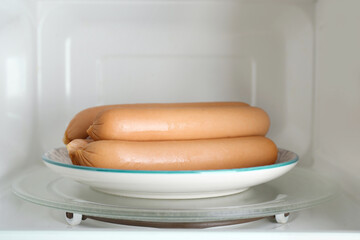 Tasty sausages on plate in microwave oven. Meat product
