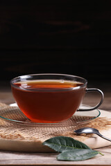 Aromatic hot tea in glass cup and leaves on wooden table