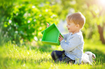 Smiling child sitting on the spring meadow with model of the green house in his hands.