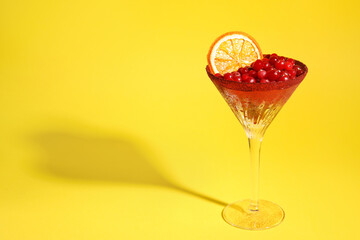 Martini glass with cranberries and dry orange slice on yellow background. Space for text