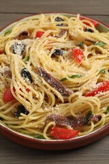 Plate of delicious pasta with anchovies, tomatoes and parmesan cheese on wooden table, closeup