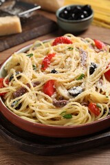 Delicious pasta with anchovies, tomatoes and parmesan cheese served on wooden table, closeup