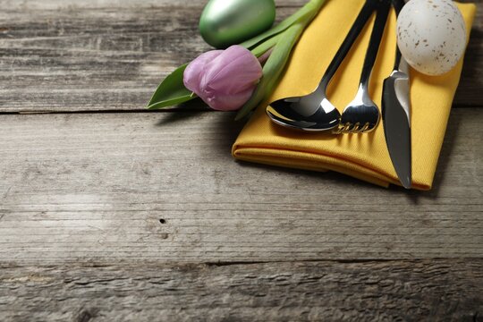 Cutlery set, painted eggs and beautiful flower on wooden table, closeup with space for text. Easter celebration