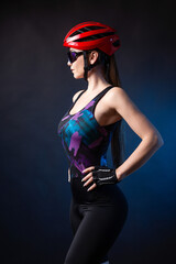 A young female cyclist wearing a safety helmet and glasses, dressed in a bib shorts poses against a...