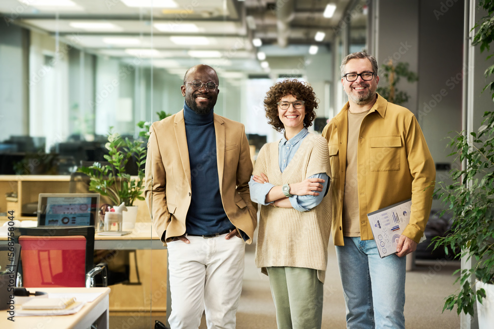 Poster three successful managers or brokers in smart casualwear looking at camera while standing in openspa
