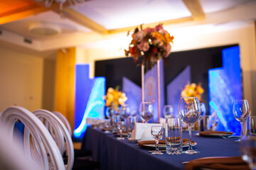 Festive Christmas, wedding, birthday table setting with blue tablecloth, orange napkin cutlery, white plates, glasses for wine, water and strong alcoholic beverages.