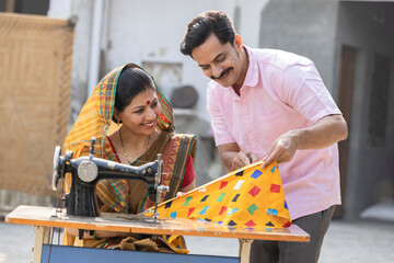 Indian rural woman using sewing machine and her husband.