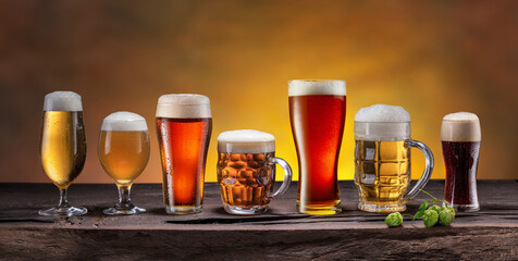 Collection of different beer glasses and beer types on old wooden table.