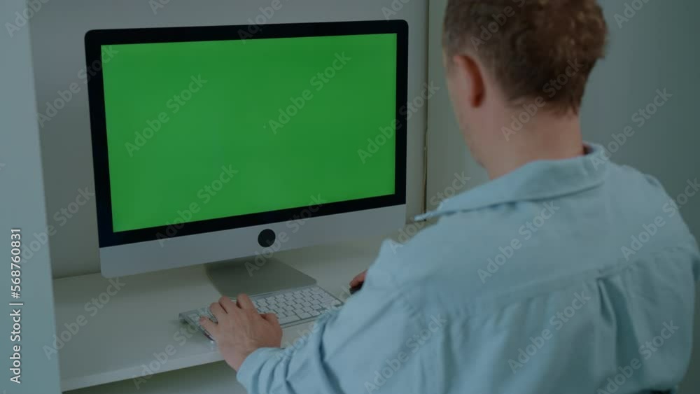 Poster manager works in the office rear view man sitting at the workplace typing on white keyboard using computer mouse display with green screen