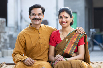 Indian rural couple sitting on traditional bed in village.