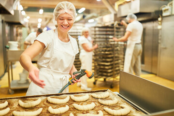Lehrling in der Großbäckerei streut Mohn auf Croissants