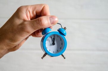 Classic arrow blue alarm clock on a man hand on white background, concept of the passage of time