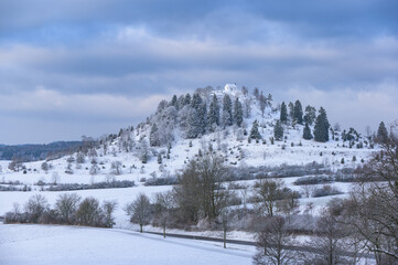 Fototapeta na wymiar Schneebedeckter Hügel mit Bäumen und Kapelle