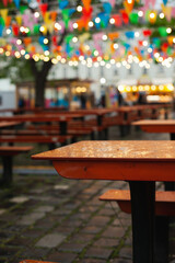 Easter market colorful flags bunting banner and lights decoration on rainy day. Festive happy birthday celebration background. Empty tables on rainy day at spring fair.