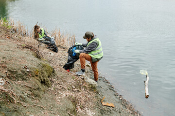 Couple cleaning lake shore and putting garbage in plastic bags