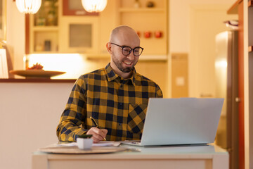 Fototapeta premium Portrait of young Caucasian man wearing glasses smiling and working on laptop. Worker using computer. Concept of remote work and freelance
