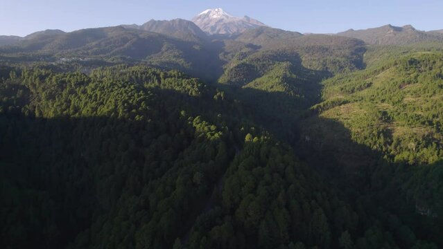 Drone video of a highway across the forest in the hills near the Pico de Orizaba volcano, with the volcano in the background