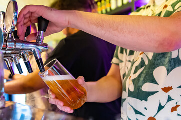 man bartender hand at beer tap pouring a draught beer in glass serving in a restaurant or pub