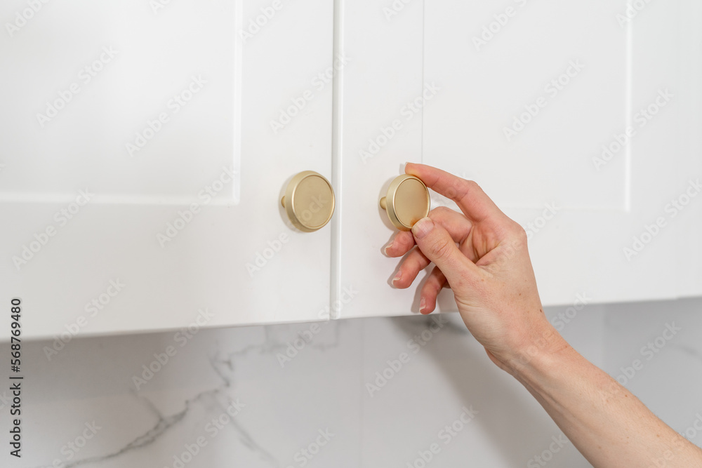 Wall mural woman open white cupboard door at kitchen, closeup