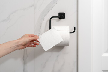 hand taking a new tissue from roll hanging in restroom