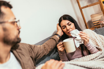 Sick young couple drinking hot tea and blowing nose at home - health, flu and people concept