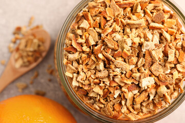 Jar of dried orange zest seasoning and fresh fruits on light grey table, closeup