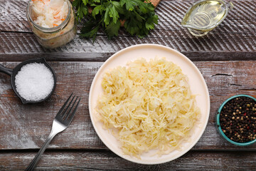 Plate of tasty sauerkraut and ingredients on wooden table, flat lay