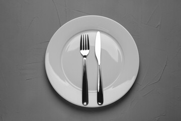 Empty plate and cutlery on grey textured table, top view