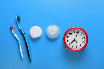 Containers with dental floss, toothbrushes and alarm clock on light blue background, flat lay