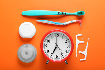 Flat lay composition with dental flosses, alarm clock and different teeth care products on orange background