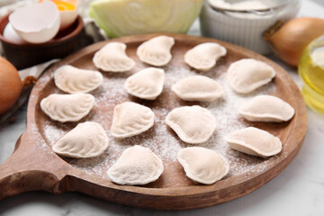 Fototapeta na wymiar Raw dumplings (varenyky) with tasty filling and flour on wooden board, closeup