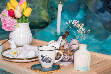 Romantic Easter table setting with candles, a white knitted plate, a cup with a drink. Table decoration with rabbit, and painted eggs
