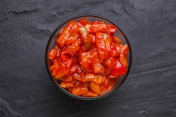 Delicious lecho in glass bowl on black table, top view