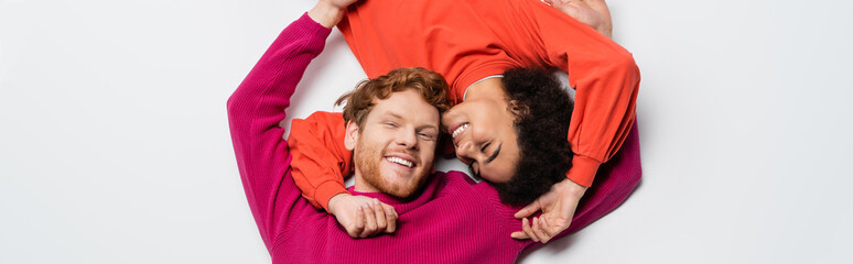 top view of happy redhead man and cheerful african american woman hugging each other on white, banner.