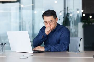 Fototapeta premium Asian businessman sick working at workplace inside office with laptop, man in shirt and glasses coughs and has a cold.