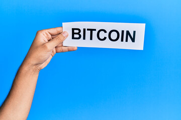 Hand of caucasian man holding paper with bitcoin word over isolated blue background