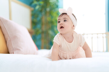 Adorable toddler sitting on bed with relaxed expression at bedroom
