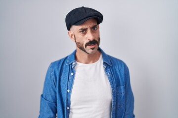 Hispanic man with beard standing over isolated background skeptic and nervous, frowning upset...