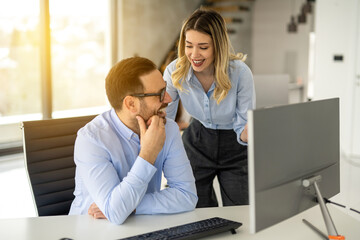Cheerful business woman and man having conversation during meeting in front of computer at modern office.