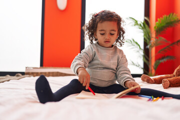 Adorable hispanic girl drawing on notebook sitting on sofa at bedroom